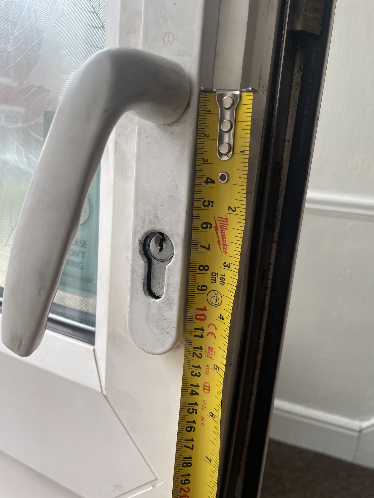 Measuring a uPVC door lock with a tape measure before ordering the replacement